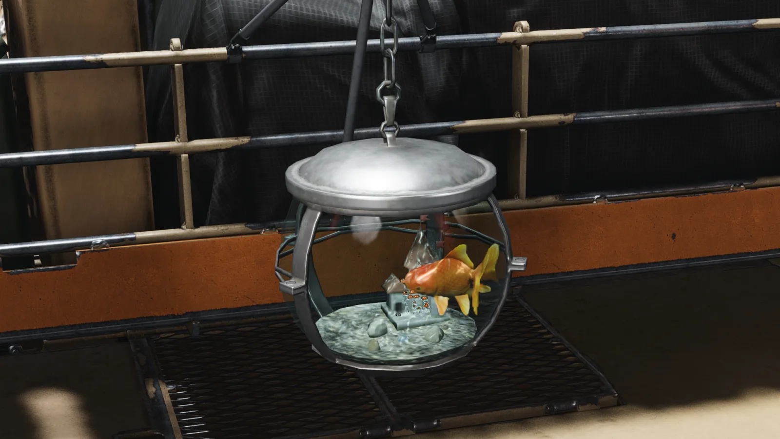 A charm shaped like a small round bowl holding a goldfish, hanging by a chain from the side of a vehicle.